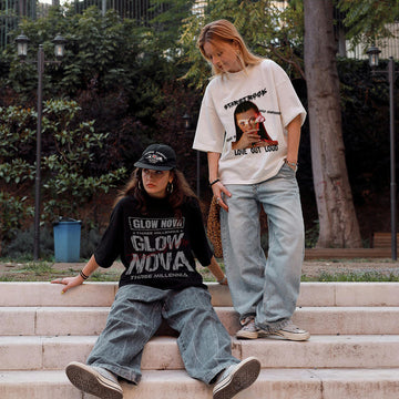 Two people wear glownova custom t-shirt and sitting on steps outdoors with trees and a fence in the background