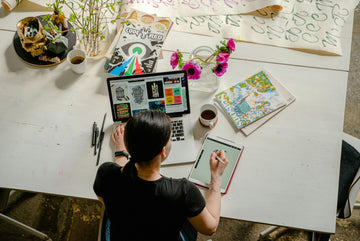 Person working at a desk with a laptop, tablet, and various items on a white table.