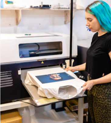 Person with blue hair using a large printer to print on a shirt.